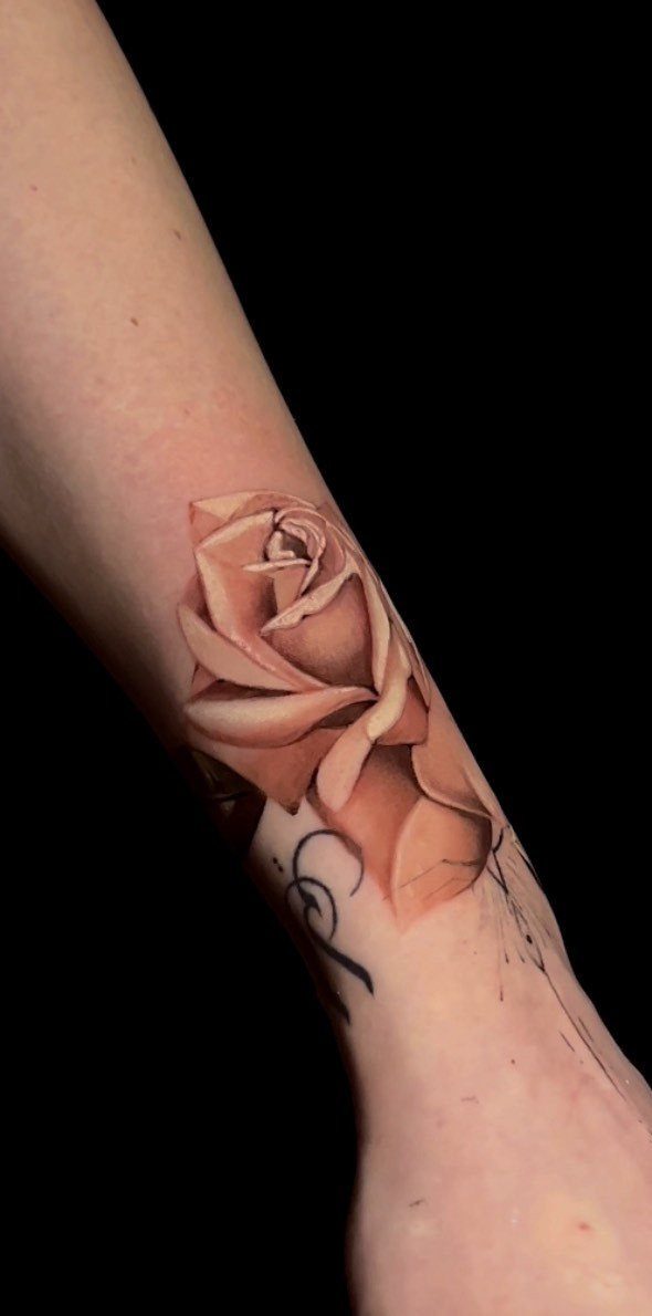 Peach-colored rose tattoo on a person's wrist with a small black swirl detail.