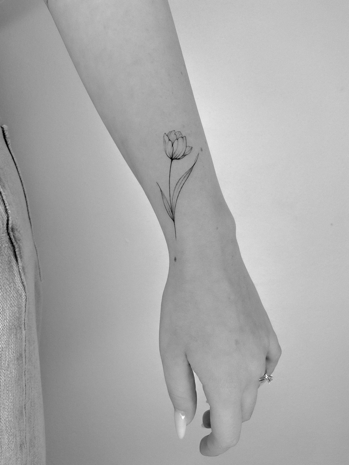 Minimalist tulip flower tattoo on a person's inner wrist in black and white.