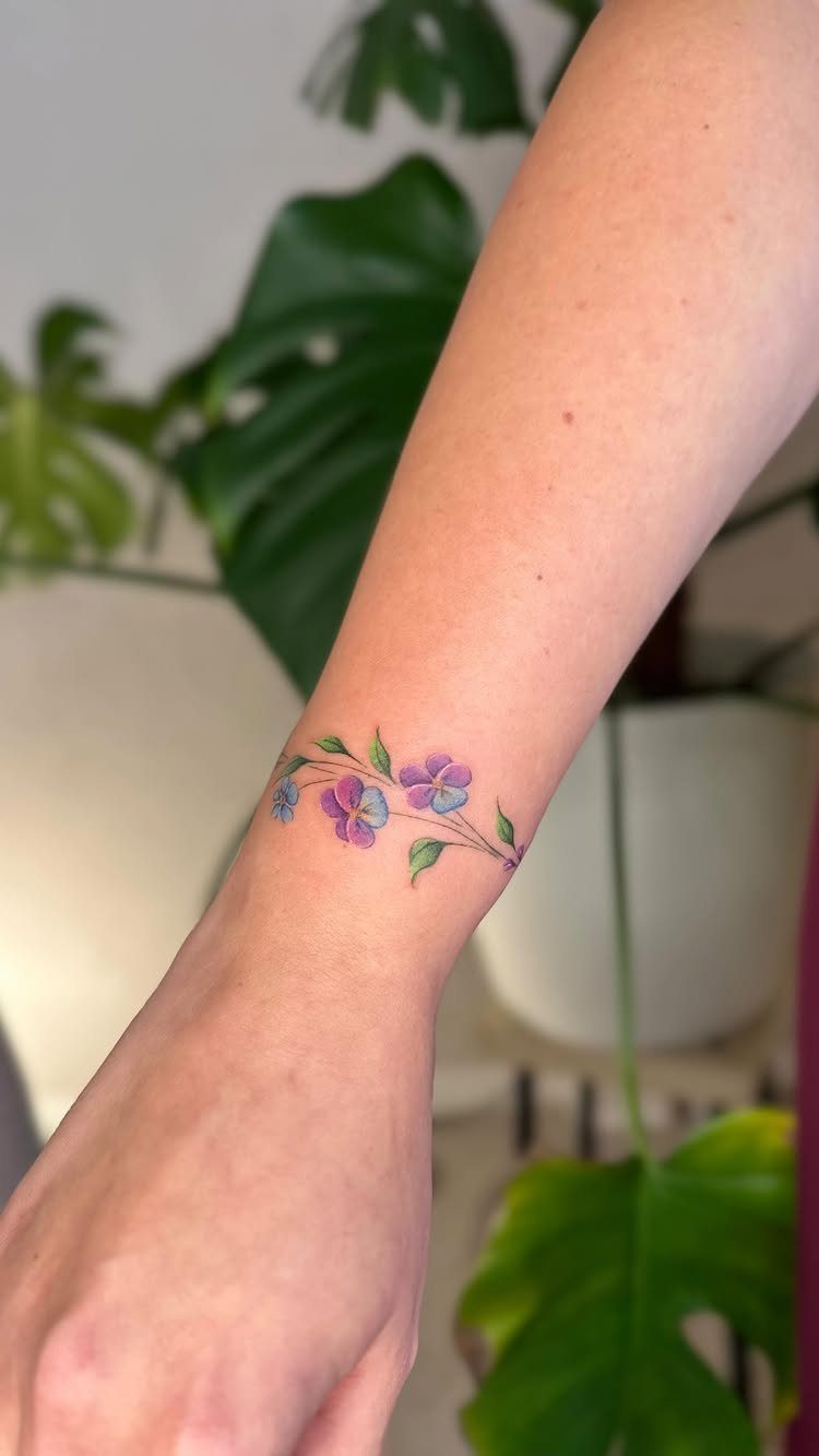 Purple flower tattoo with green leaves wrapping around a person's wrist