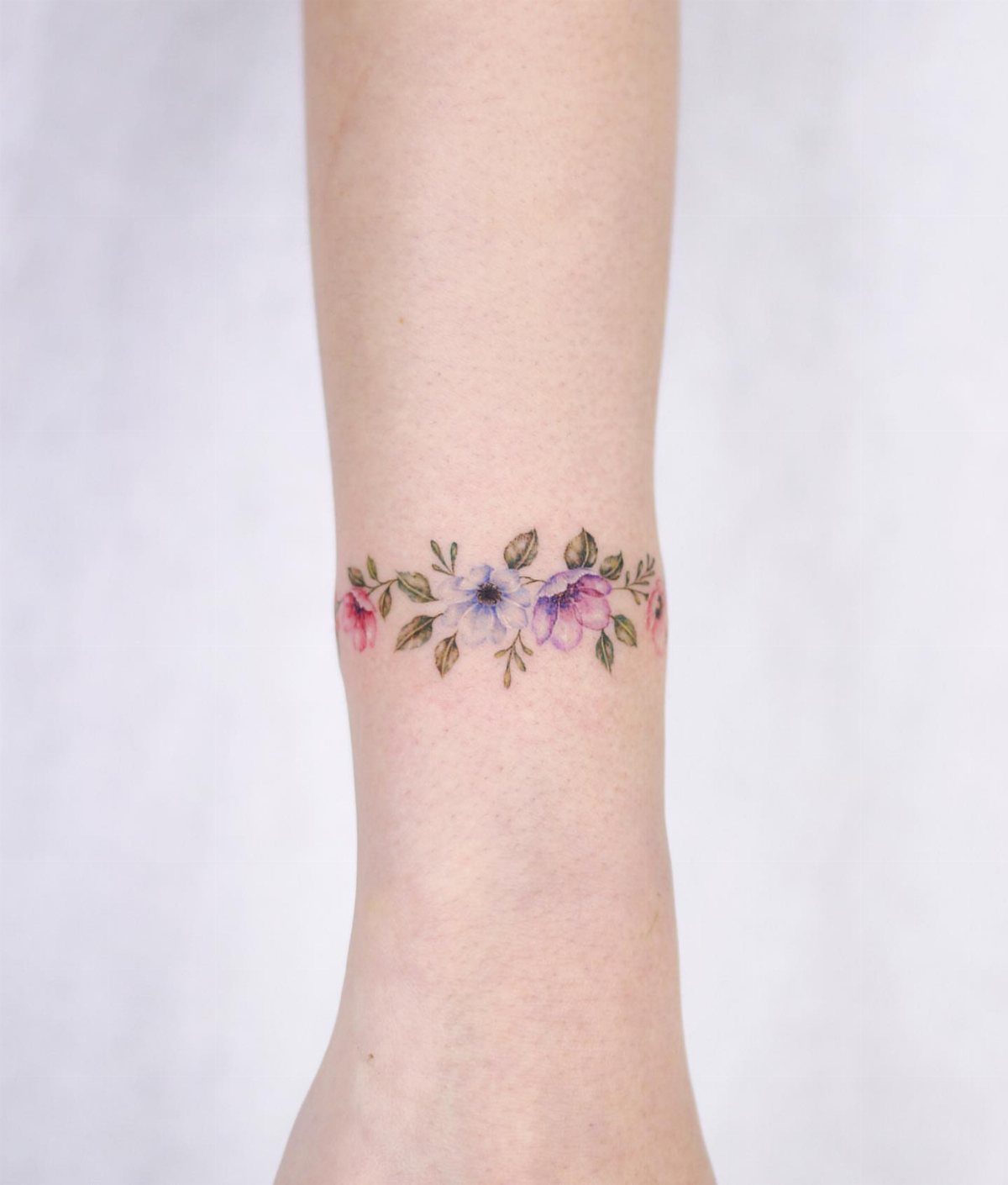Watercolor flower tattoo wrapping around a wrist with purple and pink blossoms.