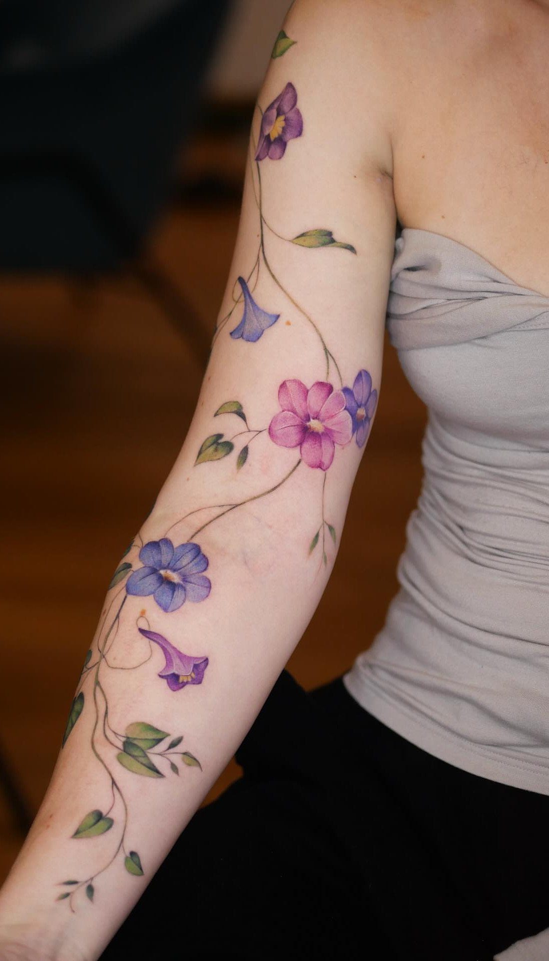 Colorful flower vine tattoo with purple and blue blossoms on a person's arm