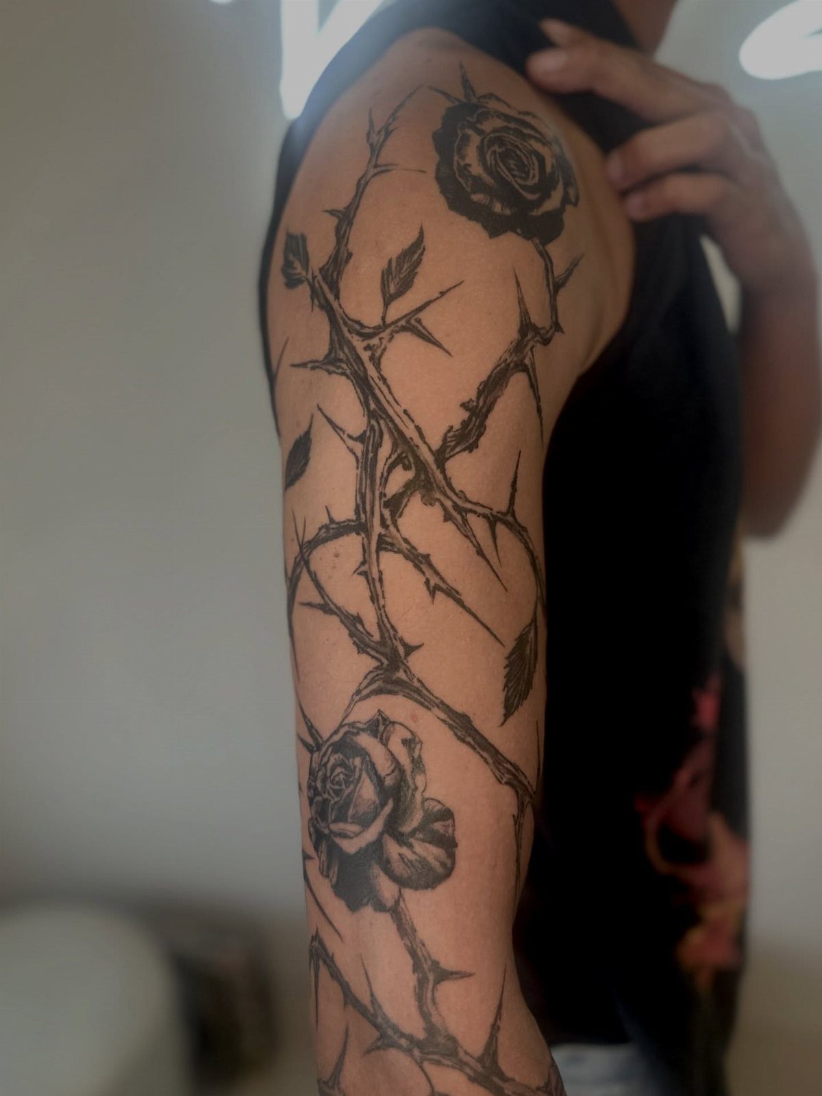 Black ink rose and thorny vine tattoo on a person's upper arm.