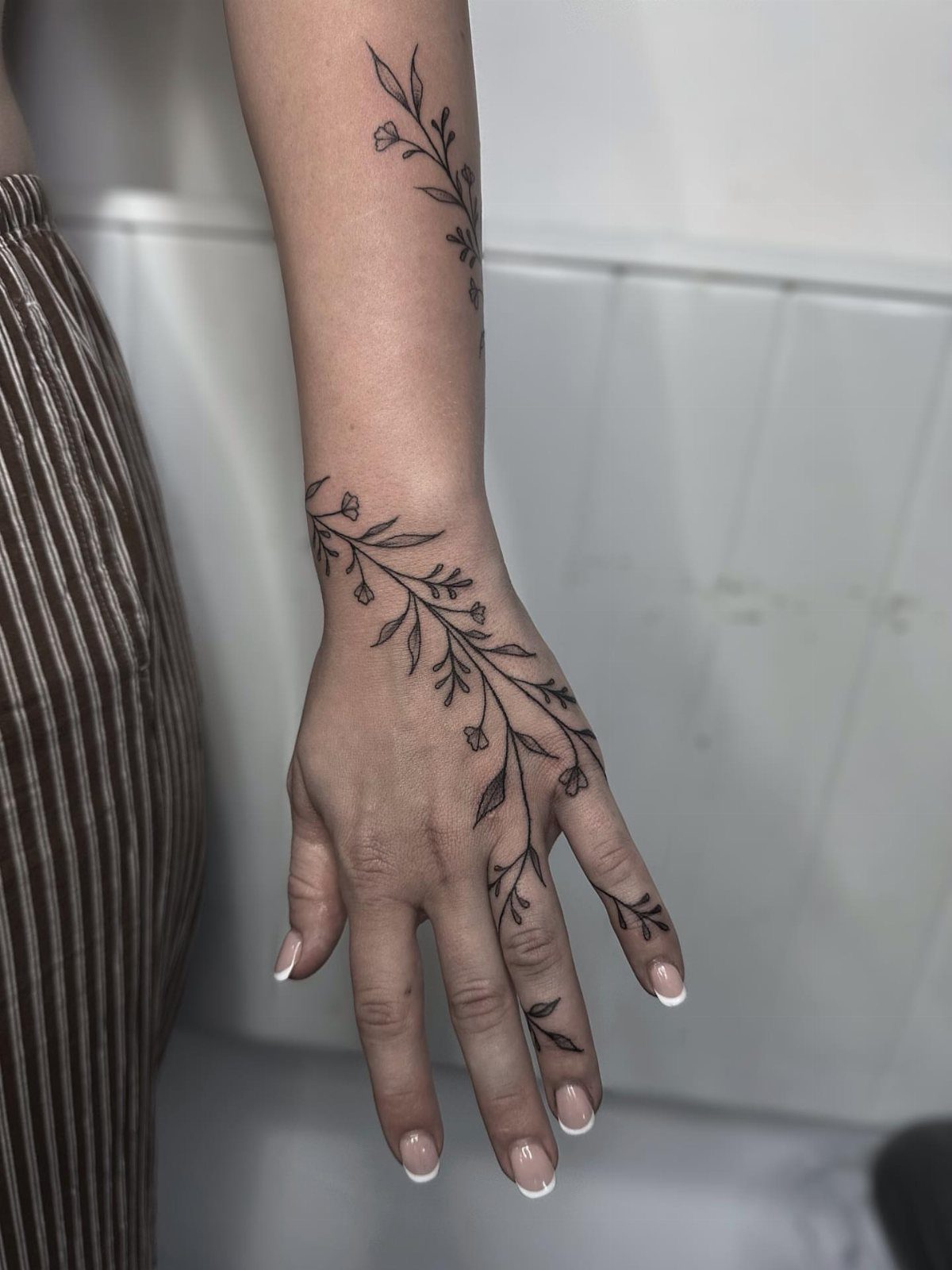 Black ink flower vine tattoo winding from the wrist across the hand and fingers.