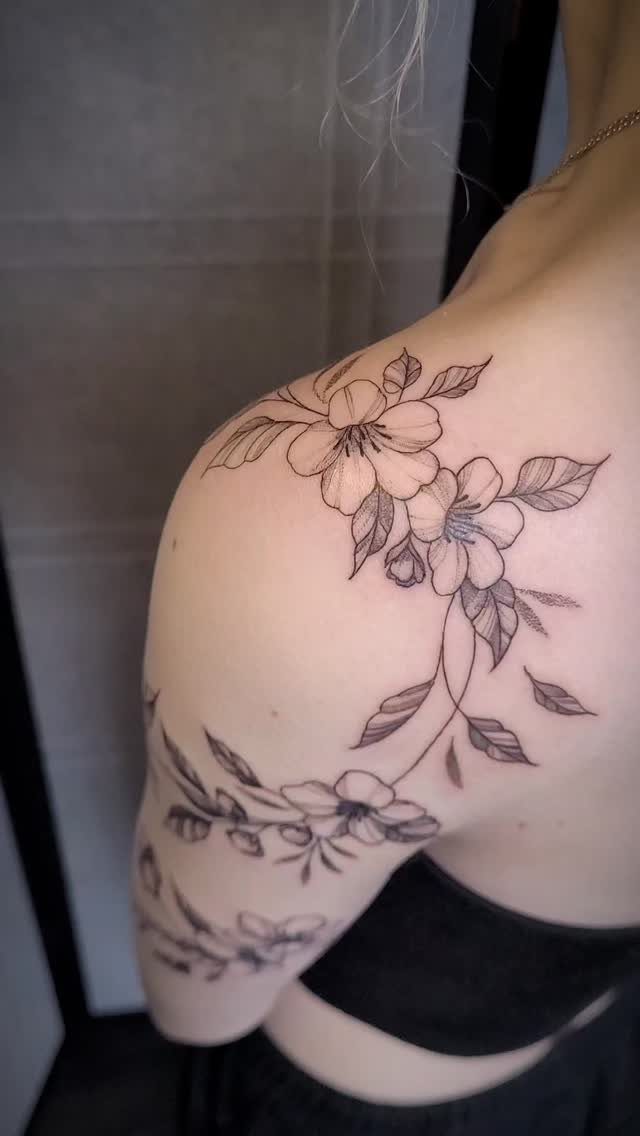 Flower and vine tattoo curving over a person's shoulder and upper arm.