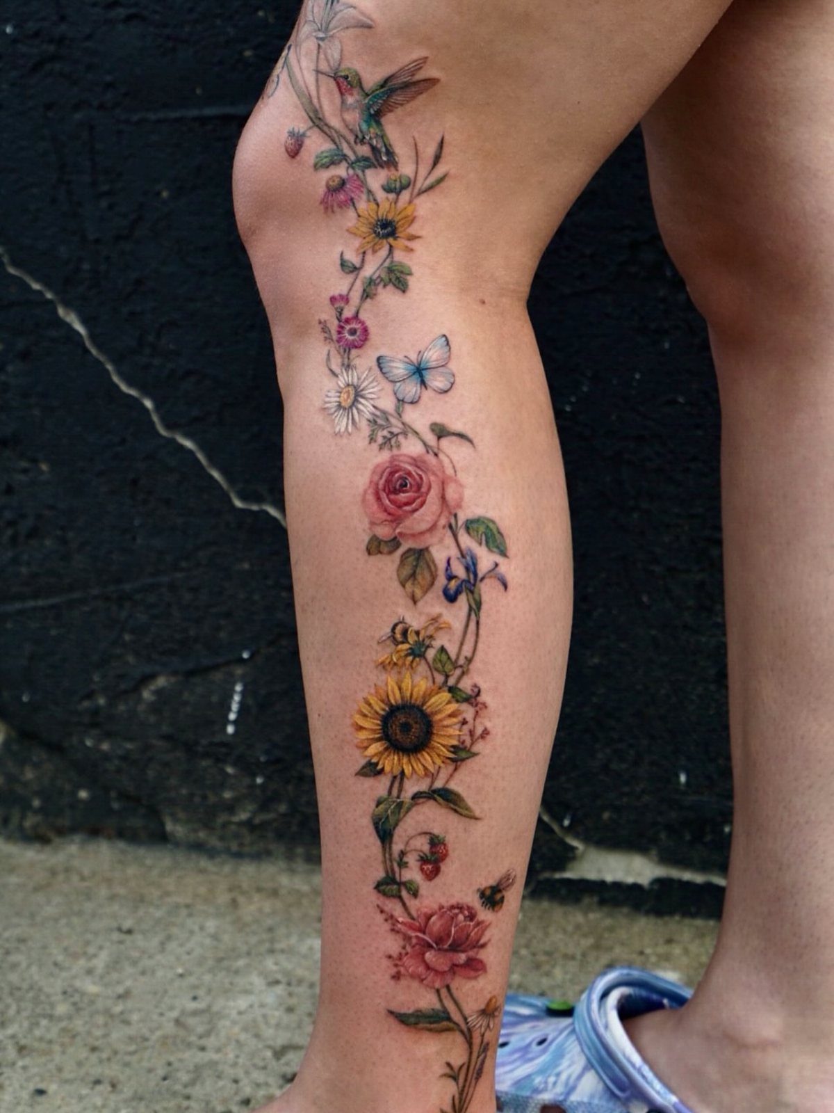 Colorful flower vine tattoo with a sunflower and butterfly on a lower leg.