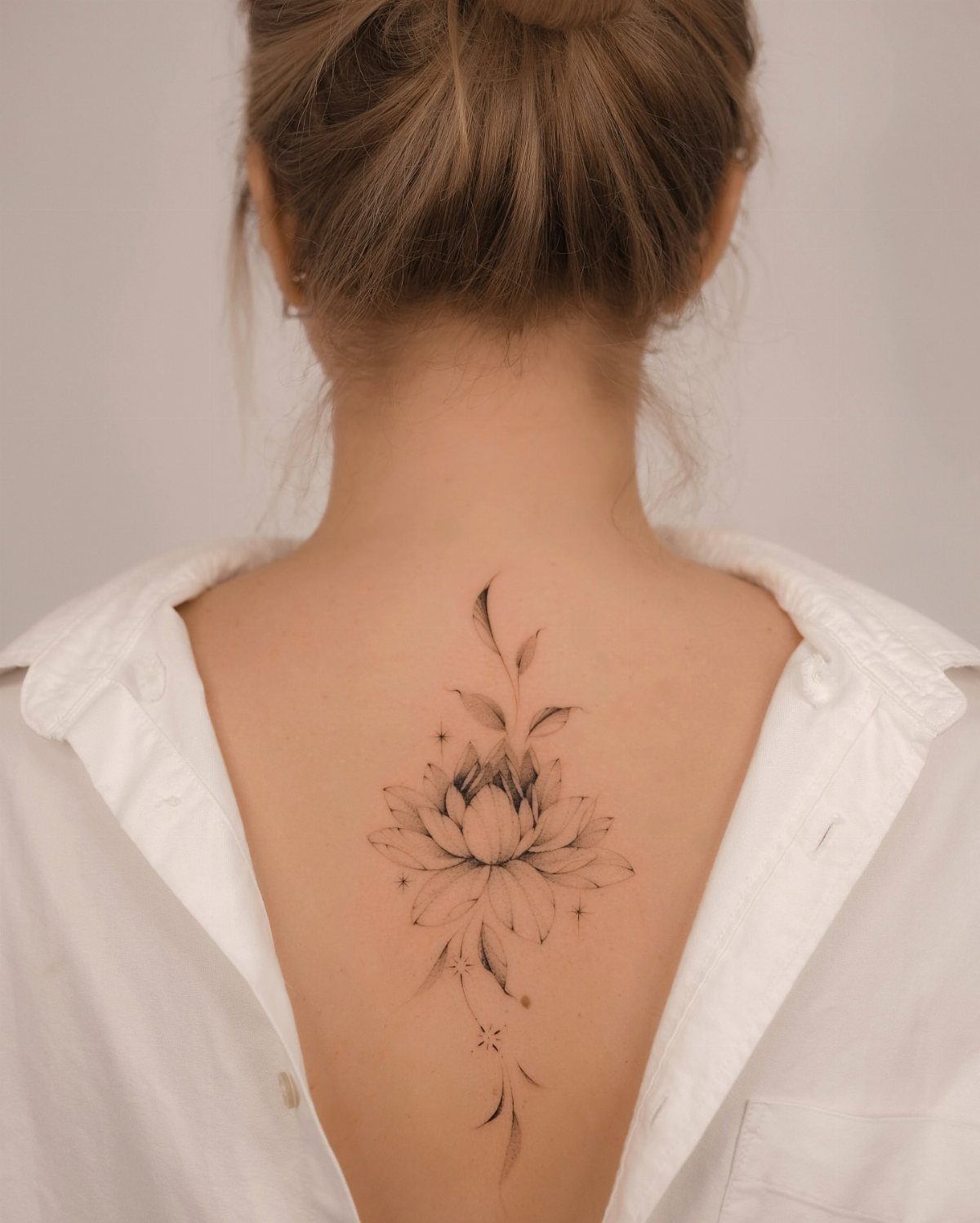 Lotus flower vine tattoo centered on the upper back of a person.