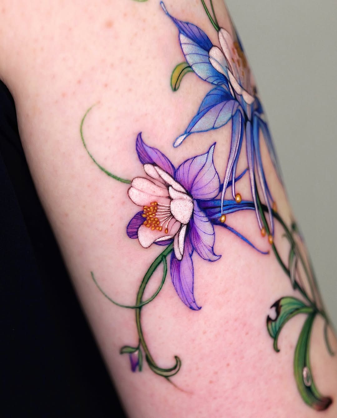 Purple and blue flower tattoo with green swirling vines on a person's arm