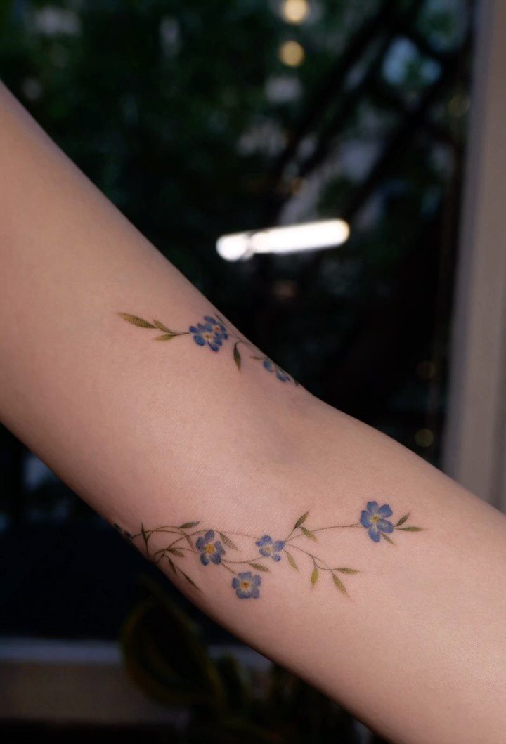 Blue forget-me-not flower tattoos with fine lines on a person's forearm.