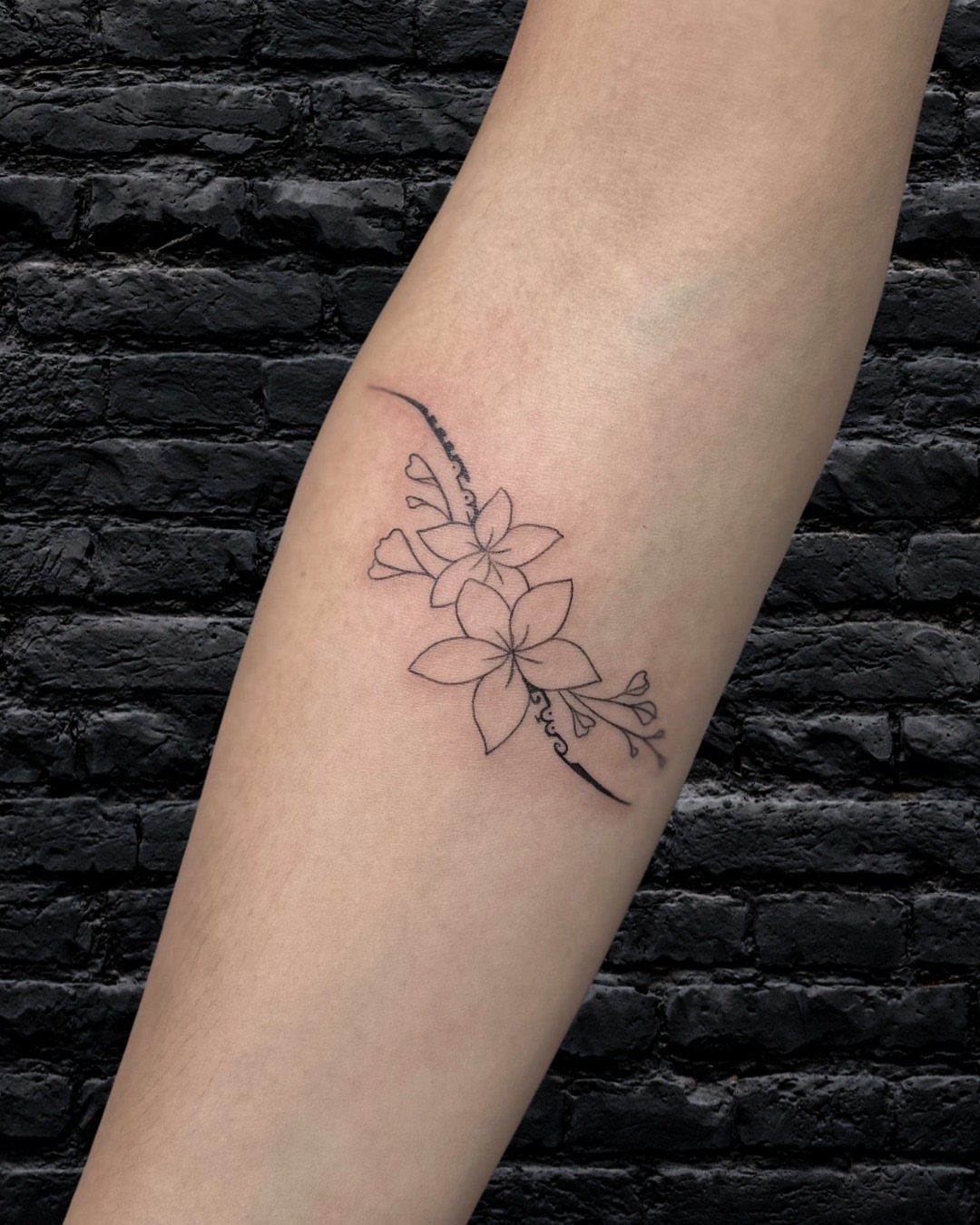 Black ink floral tattoo of tropical flowers on a person's forearm
