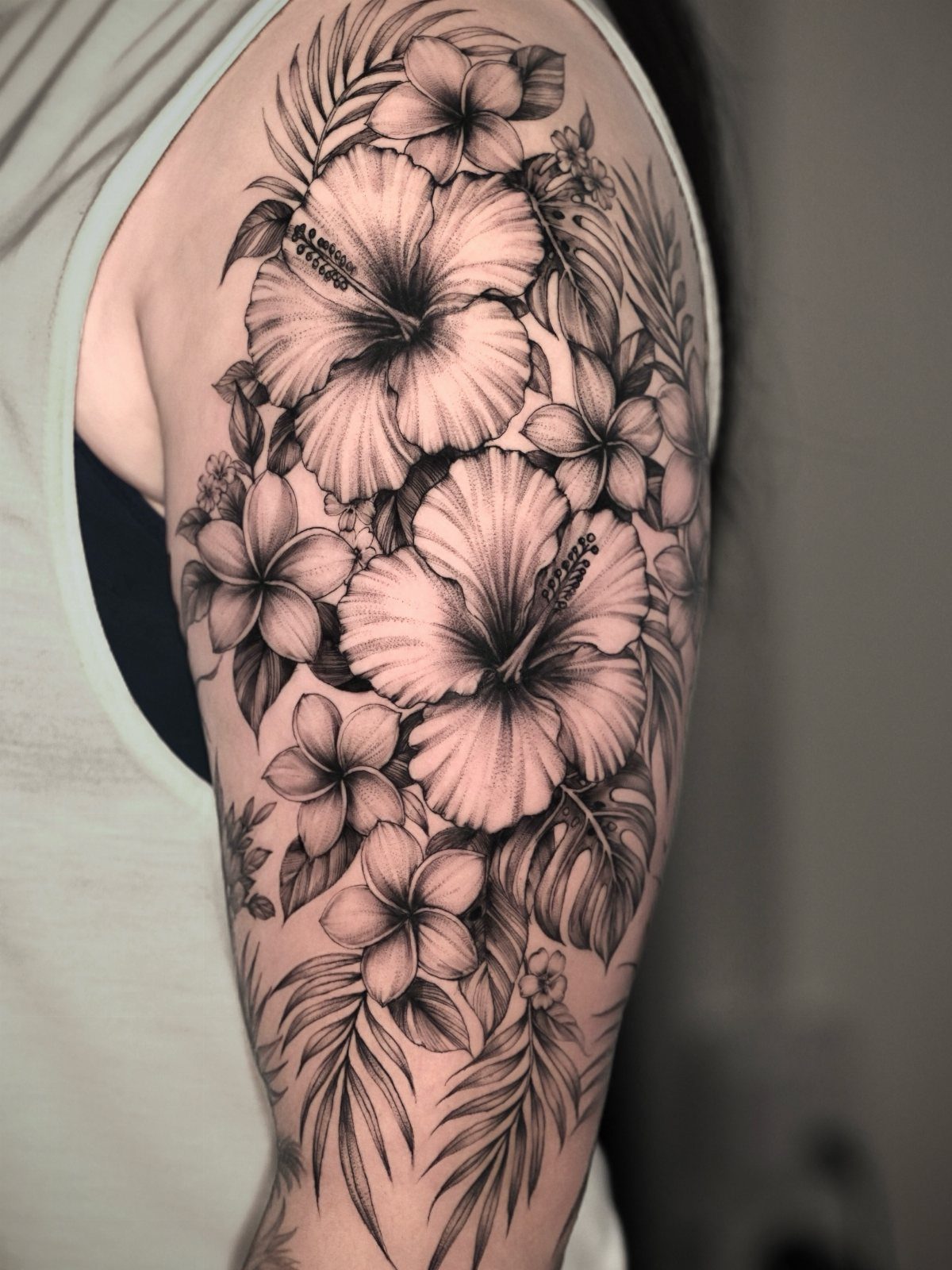 Hibiscus and plumeria flower tattoo with palm leaves on a person's upper arm