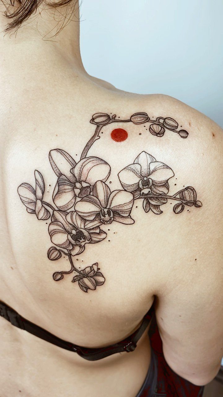 Orchid flower tattoo with a red dot on a person's upper back.