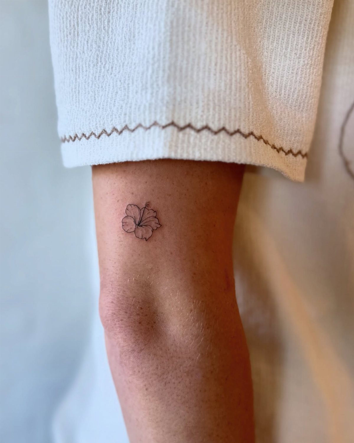 Small black ink hibiscus flower tattoo on a person's upper arm