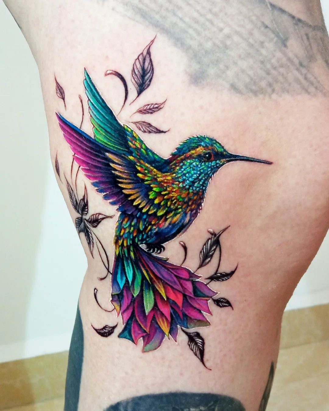 Colorful hummingbird tattoo with vibrant blue and purple feathers on a person's leg