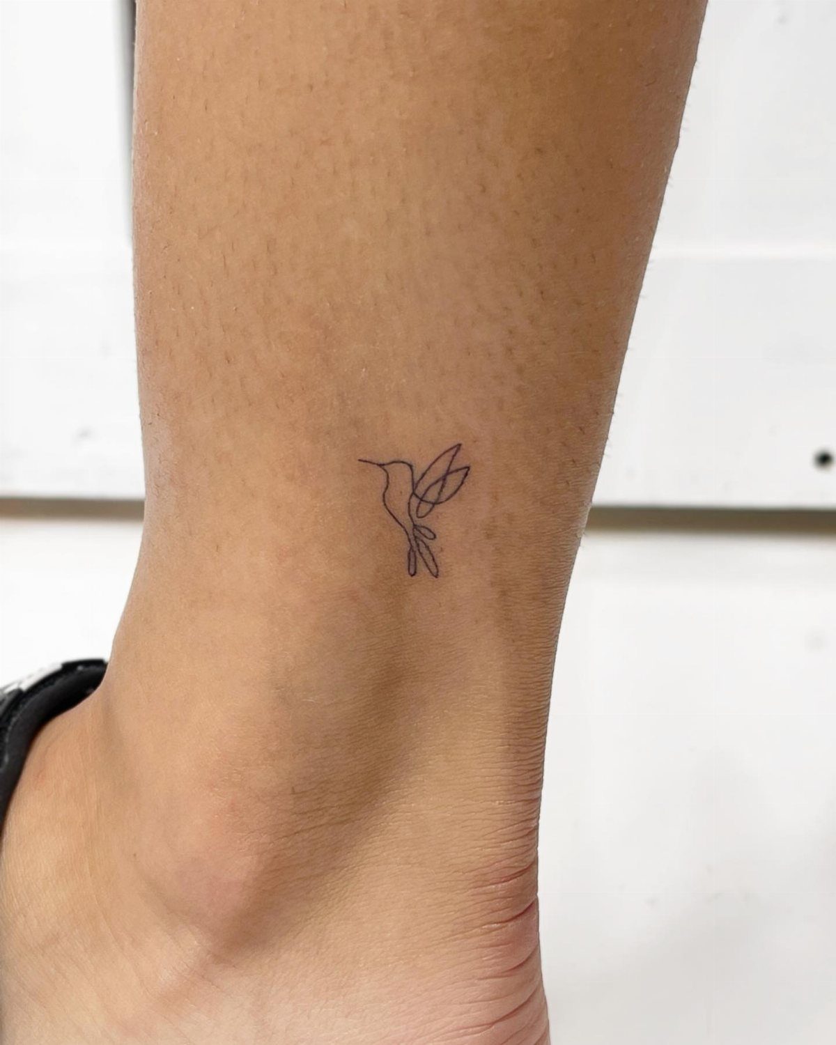 Small fine-line hummingbird tattoo in black ink on a person's ankle