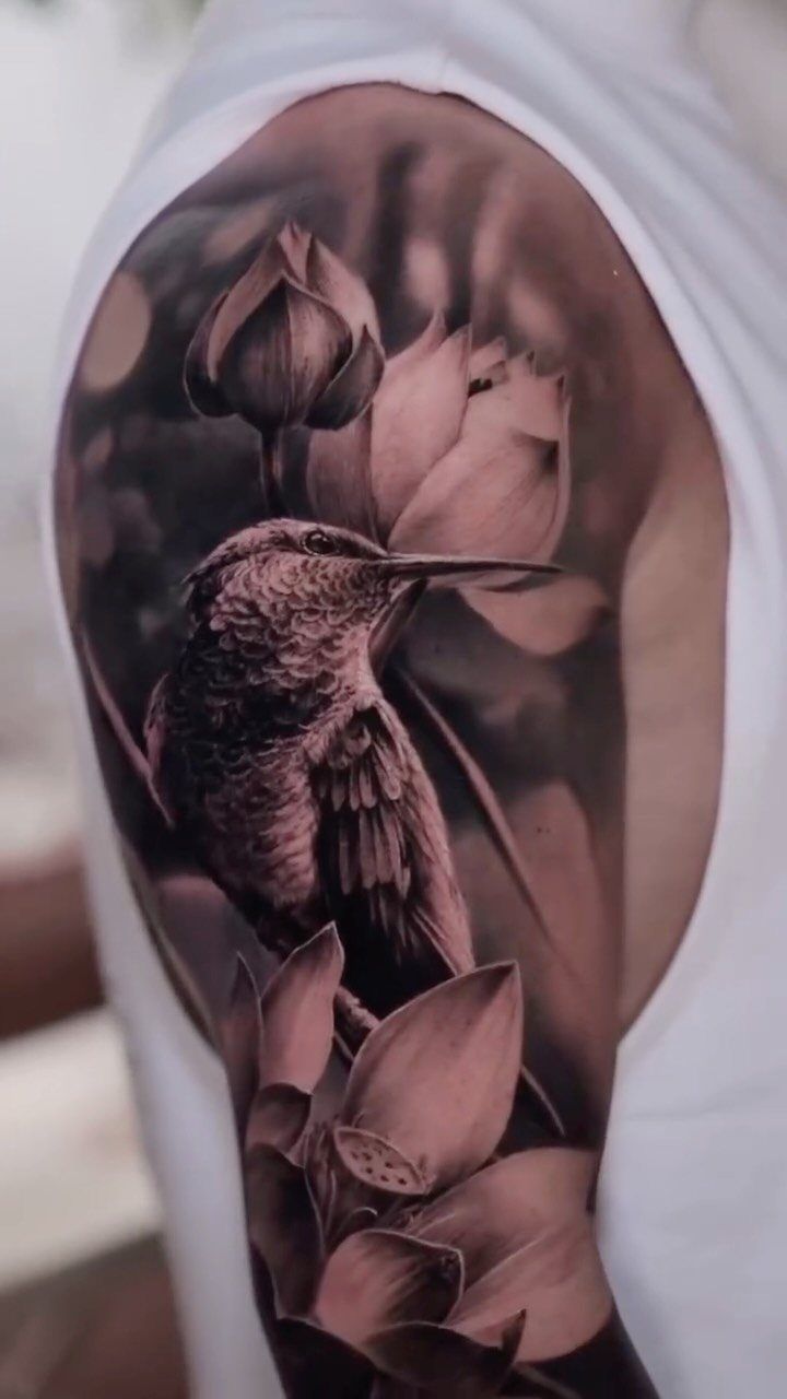 Realistic hummingbird tattoo with lotus flowers on a person's upper arm