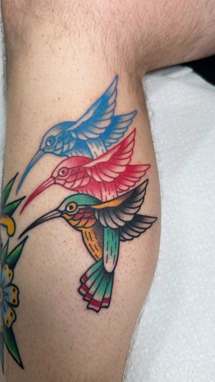 Three colorful hummingbird tattoos with bold outlines on a person's lower leg.