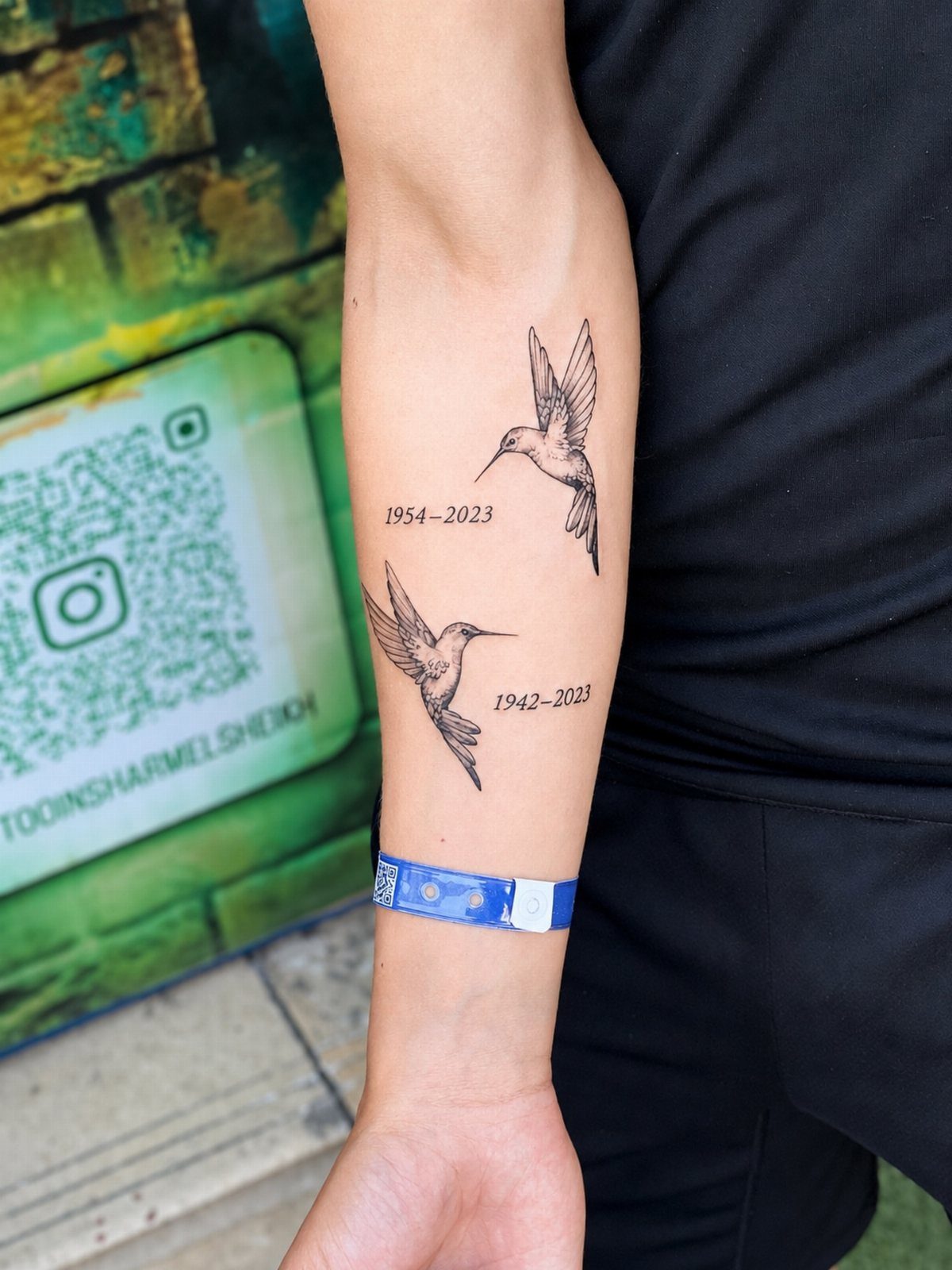 Two black ink hummingbird tattoos with dates on a man's forearm