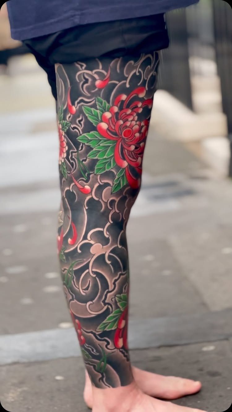 Japanese leg sleeve tattoo with red chrysanthemum flowers and dark swirling clouds.