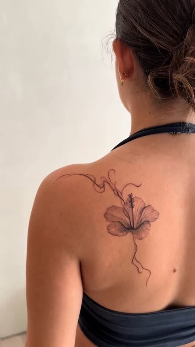 Hibiscus flower tattoo with flowing lines on a person's upper back and shoulder.