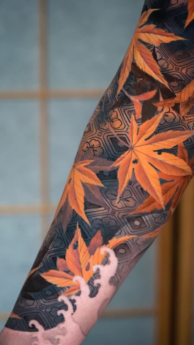 Japanese tattoo on an arm featuring orange maple leaves and crashing white waves