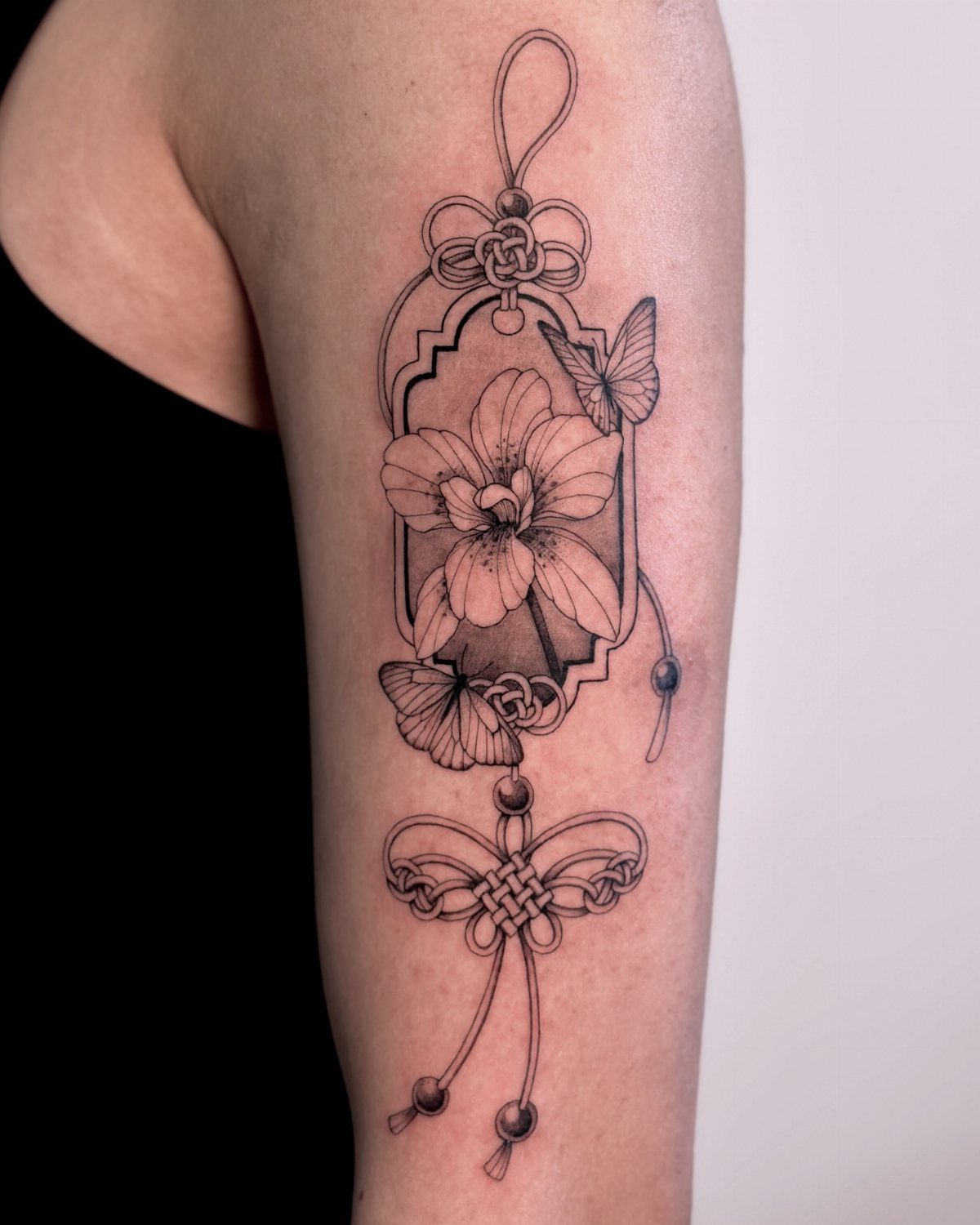Orchid flower tattoo with butterflies and ornamental knots on a person's arm