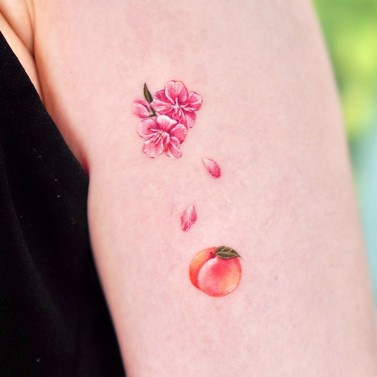 Peach blossom and fruit tattoo on a person's arm with pink petals.
