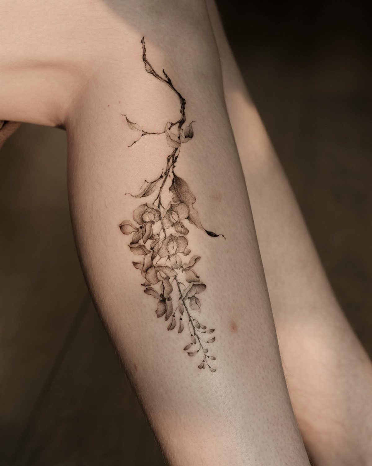Hanging wisteria flower tattoo in black ink on a person's thigh