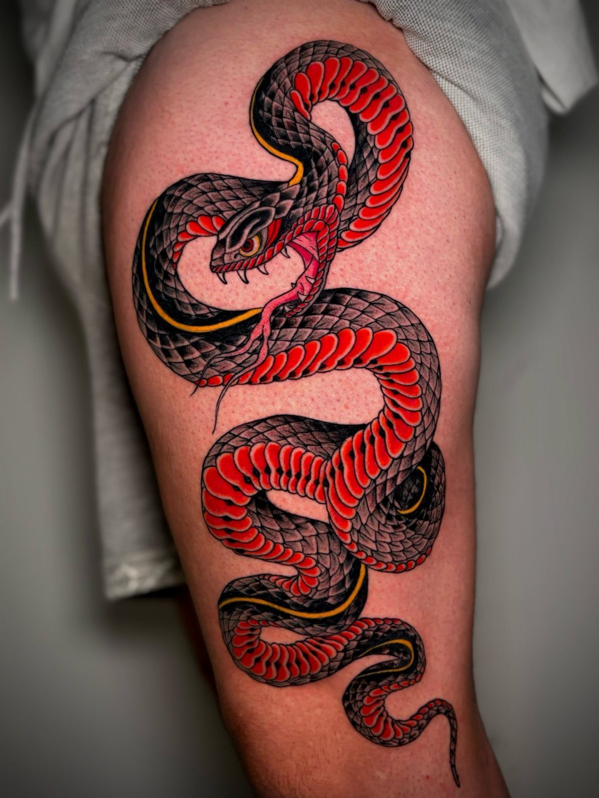 Red and black Japanese snake tattoo winding down a person's thigh.