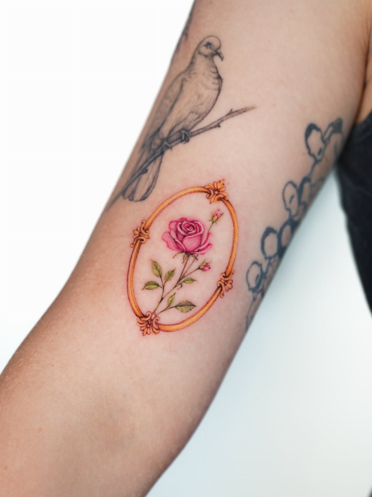 Pink rose tattoo inside a gold oval frame on a person's arm