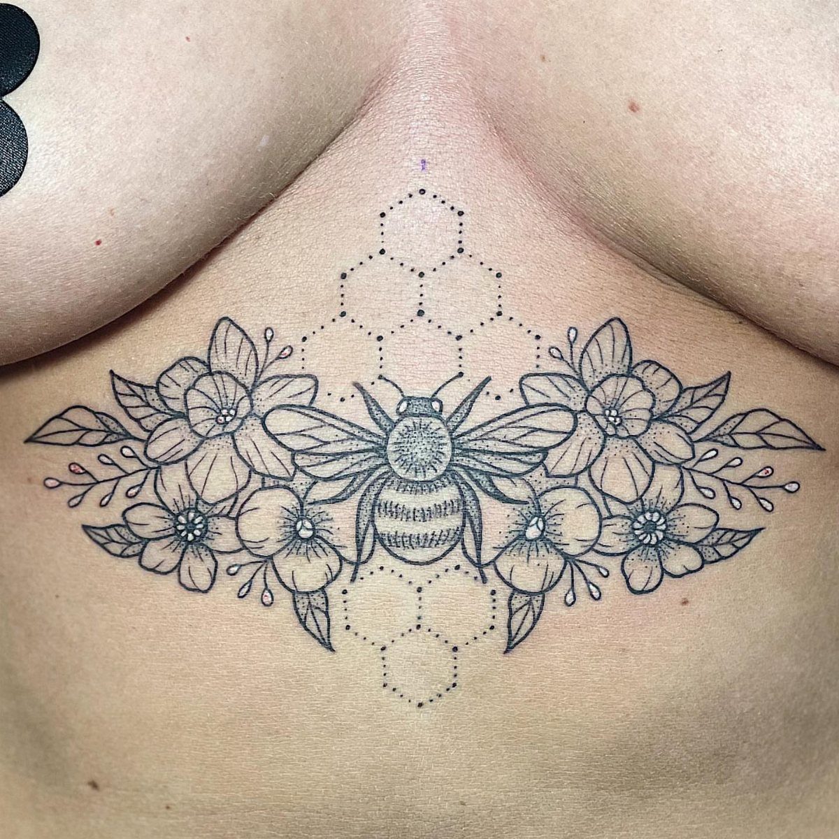 Bee and flower tattoo with honeycomb patterns on a person's sternum area.