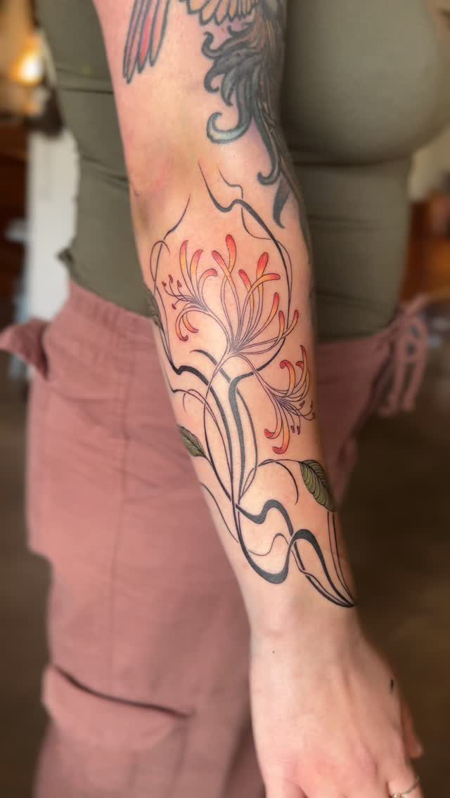 Honeysuckle flower tattoo with orange petals and black lines on a person's forearm.
