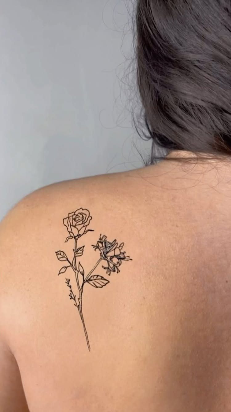 Fine line tattoo of a rose and honeysuckle on a person's upper back.
