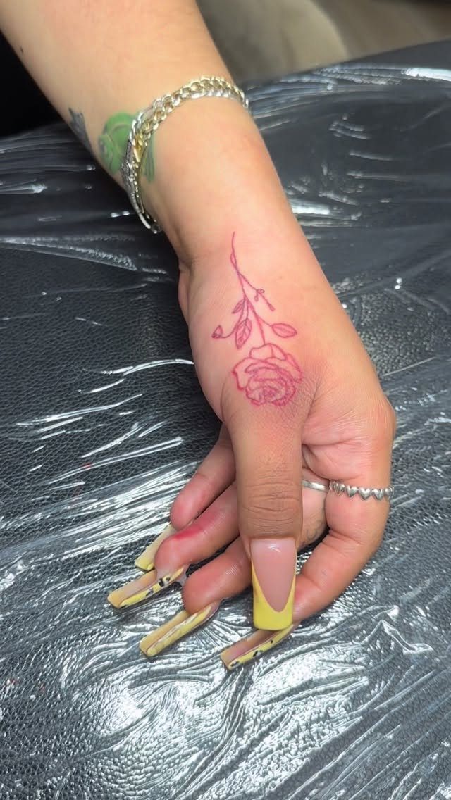 Red rose tattoo on the back of a hand with long yellow nails