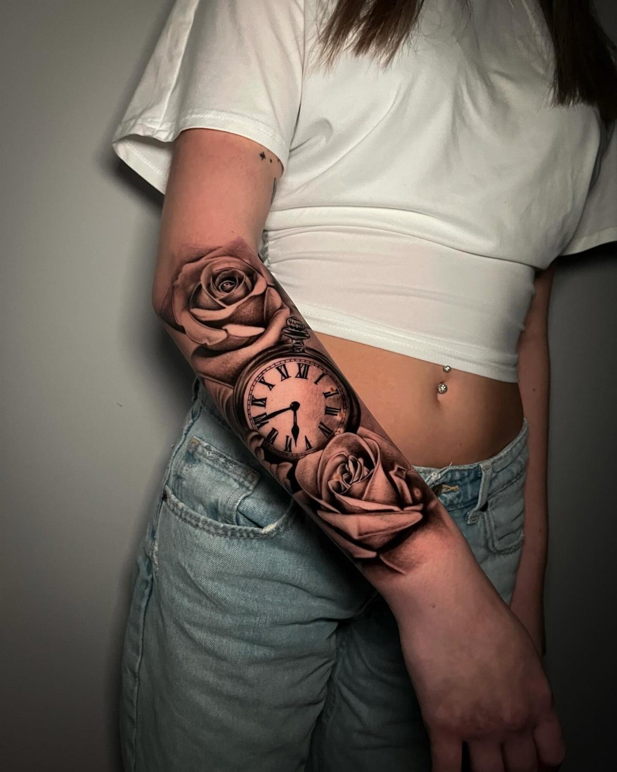 Forearm tattoo featuring a vintage clock face surrounded by two detailed roses.