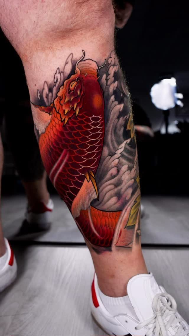 Red koi fish tattoo on a lower leg swimming upward through grey waves