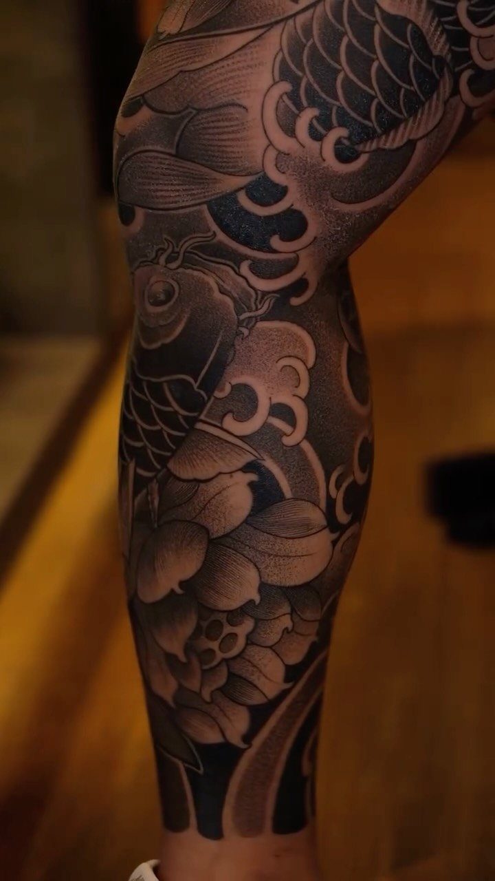 Koi fish tattoo with waves and flowers on a person's lower leg