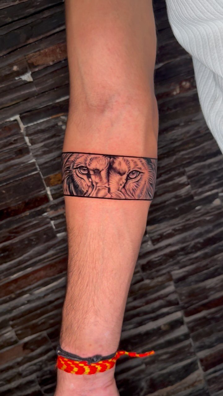 Lion face tattoo wrapped as a band around a person's forearm