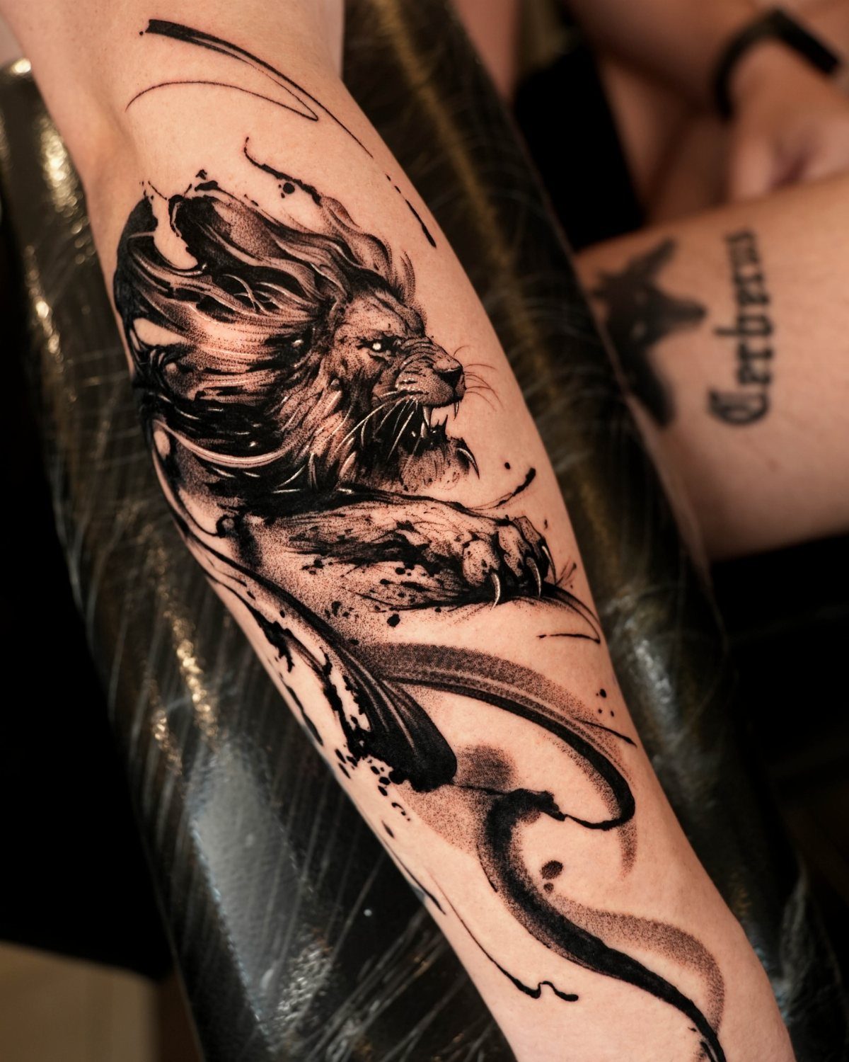 Lion forearm tattoo with a realistic face and flowing abstract black mane.