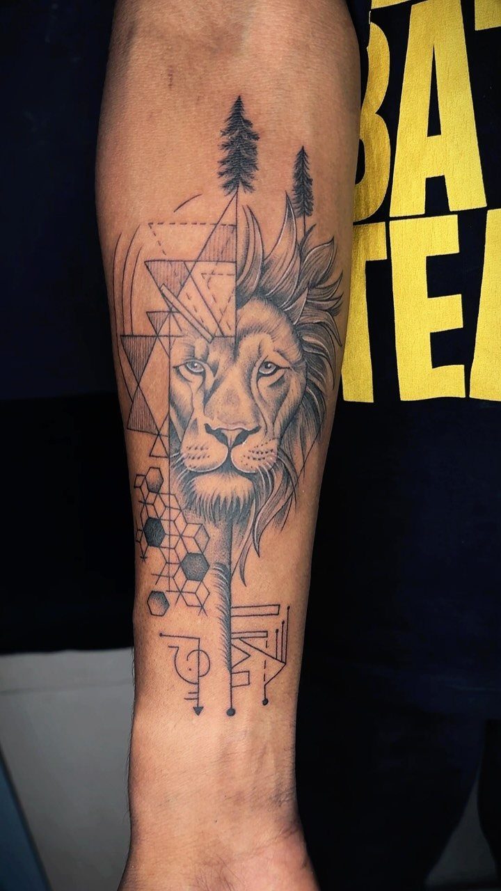 Lion forearm tattoo combining a realistic face with geometric patterns and pine trees.