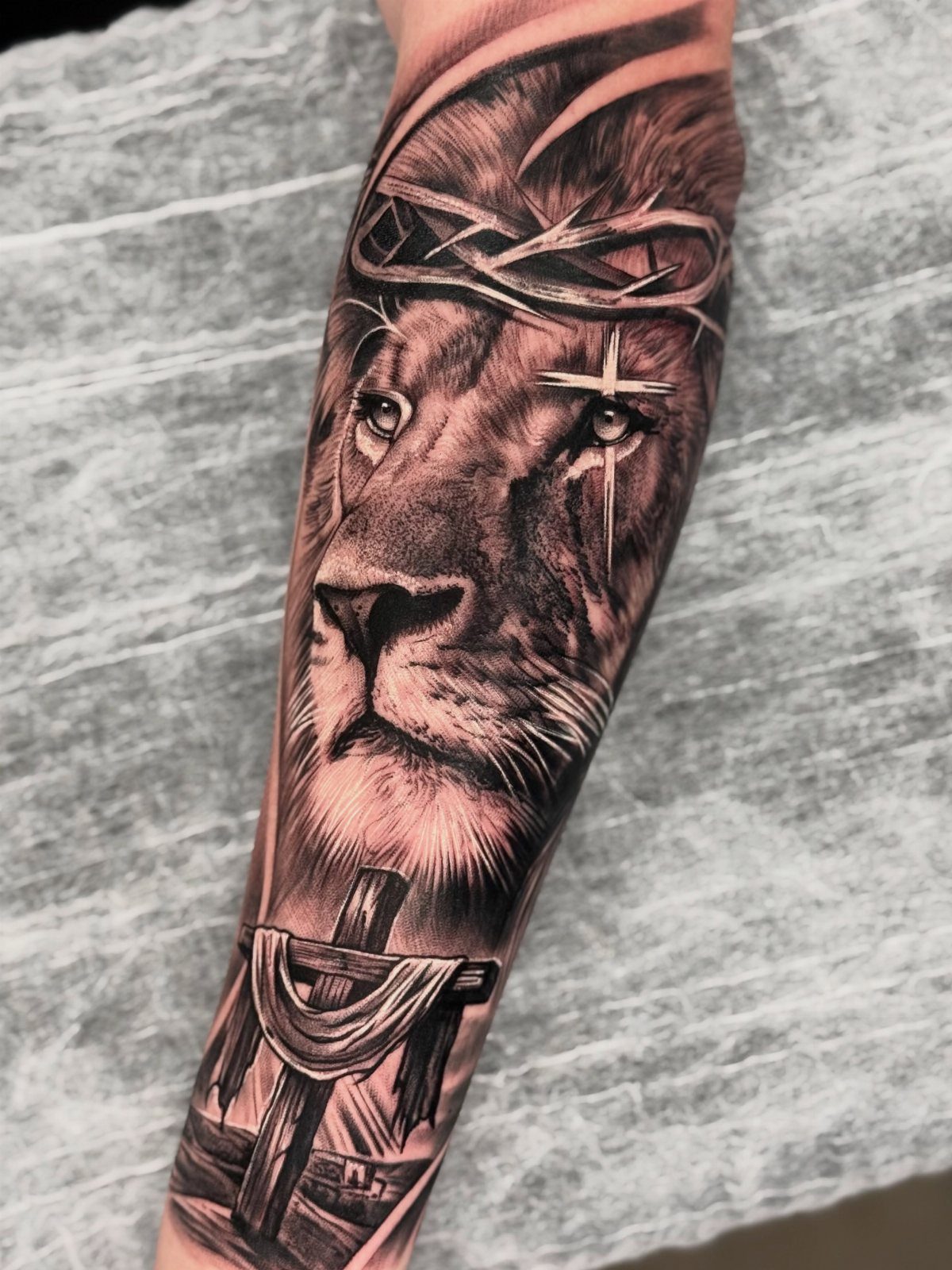 Lion forearm tattoo with a crown of thorns and a religious cross design