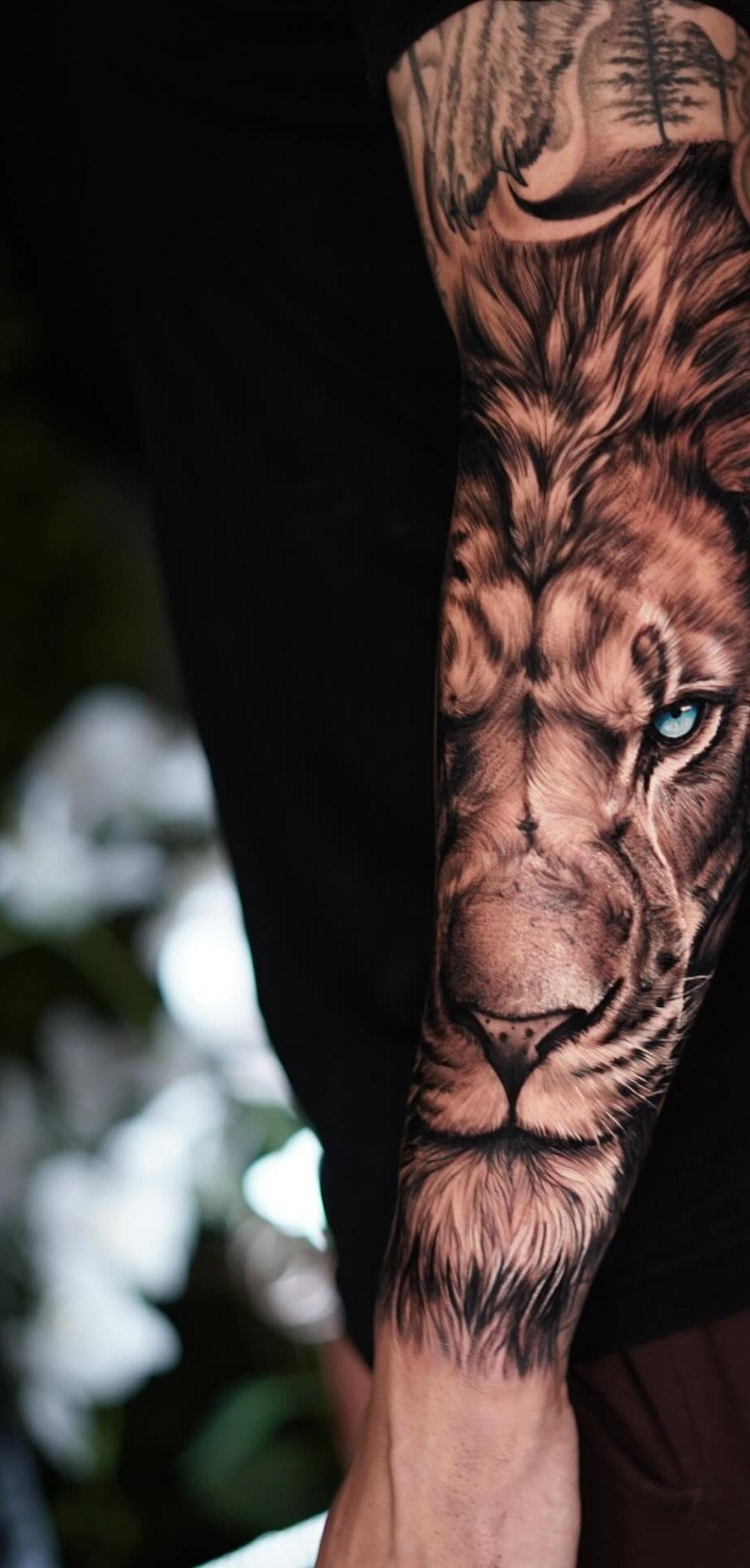 Detailed lion face tattoo on a forearm with a striking blue eye.