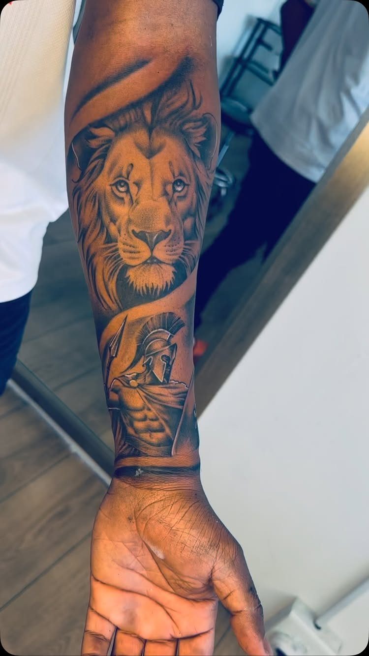 Lion and Spartan warrior tattoo on a person's forearm in black and grey ink.
