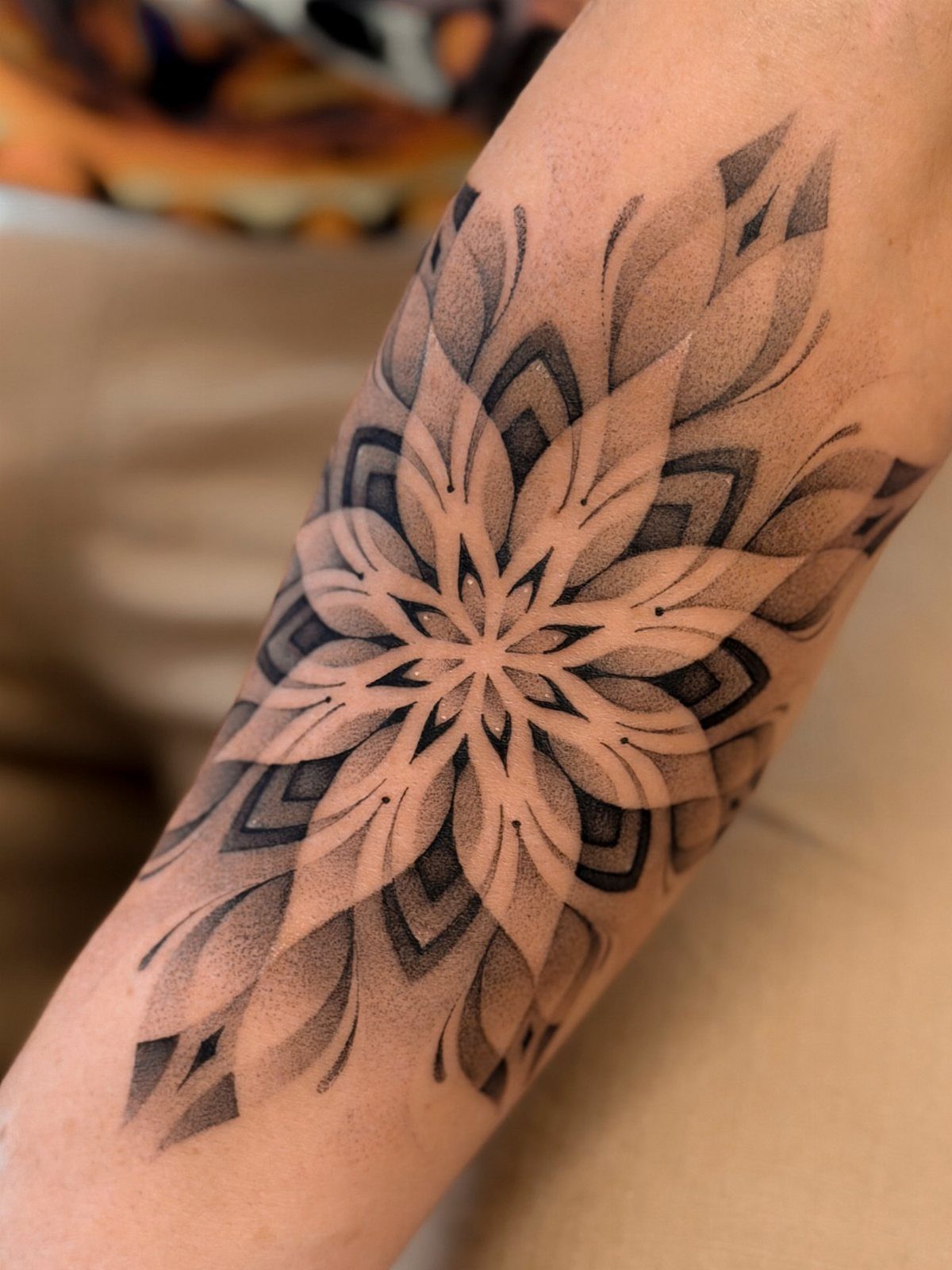 Lotus mandala tattoo in black and grey ink on a person's forearm