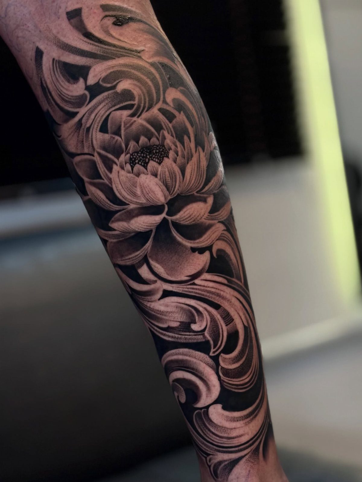 Lotus flower tattoo with ornamental swirls on a person's forearm in black ink.