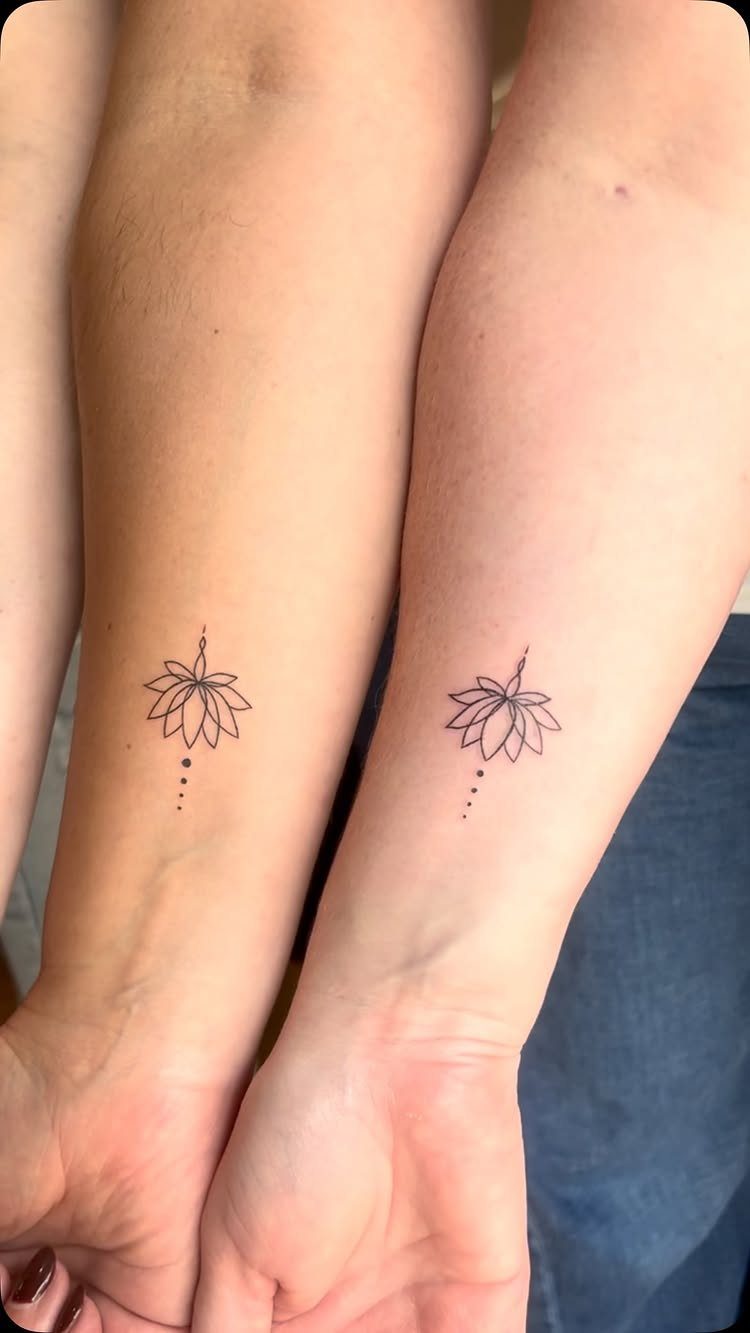 Two matching black ink lotus flower tattoos on the inner wrists of two people.