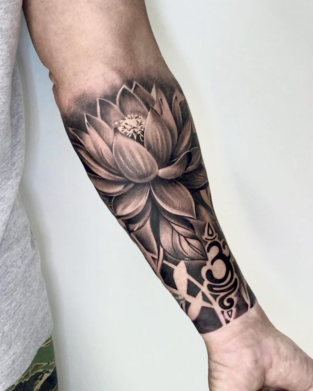 Lotus flower tattoo on a forearm with bold black tribal patterns at the wrist