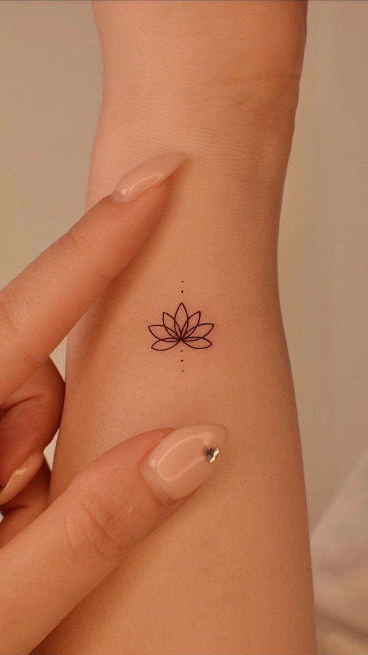 Small black lotus flower tattoo with dots on a person's inner wrist