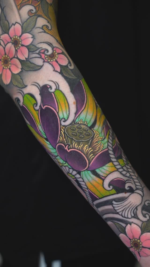 Colorful arm tattoo featuring a purple lotus flower and pink cherry blossoms with waves