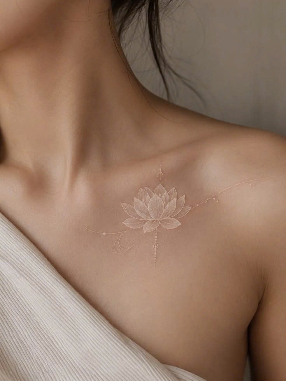 White ink lotus flower tattoo on a person's collarbone and shoulder area