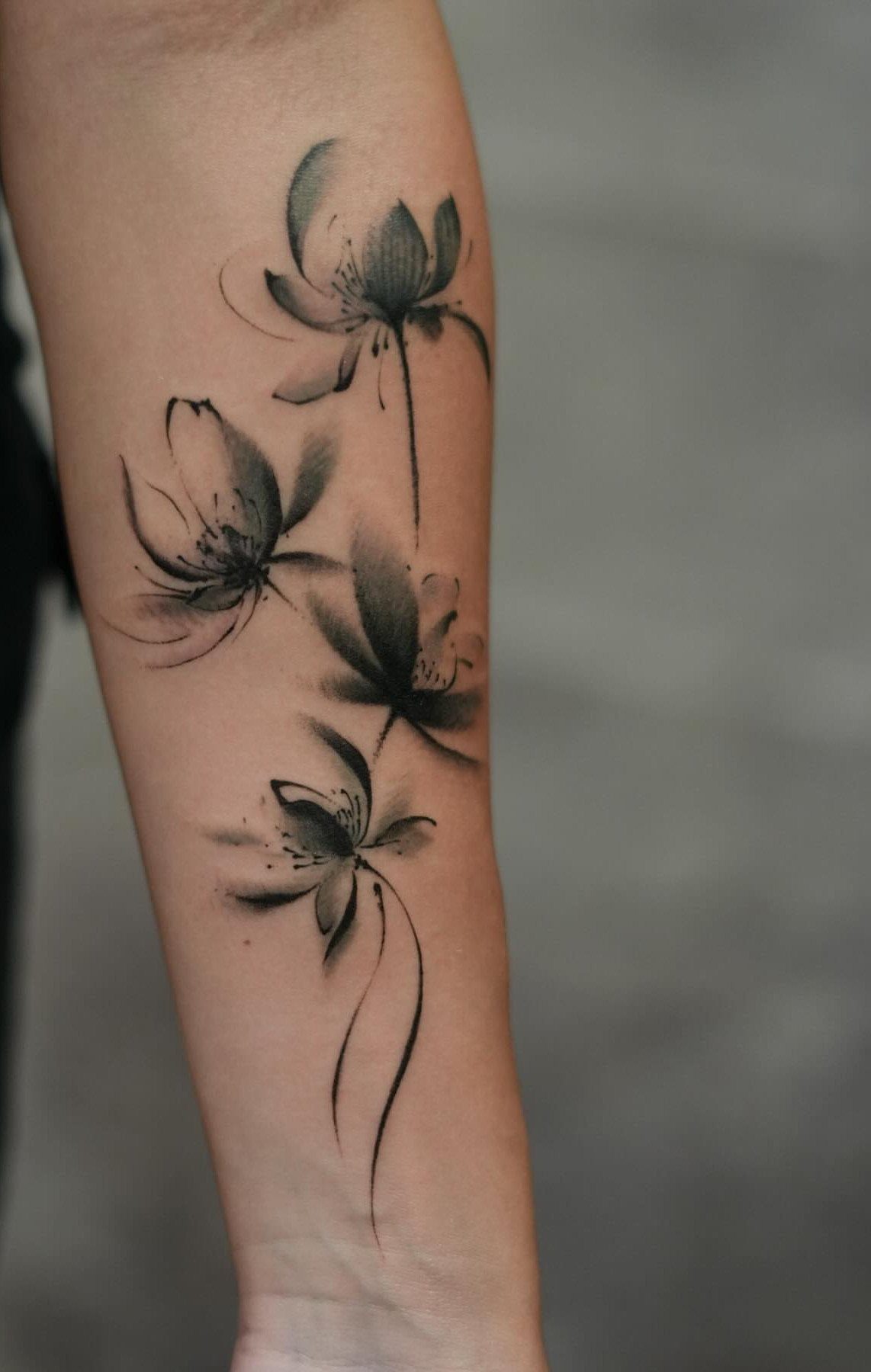 Ink wash style lotus flower tattoos on a person's forearm in black ink